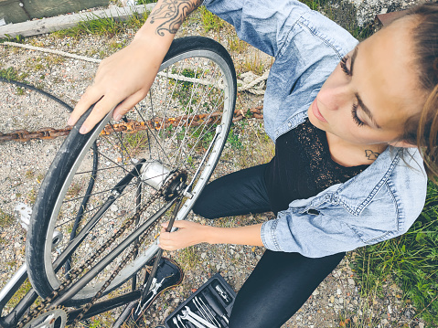 Young beautiful female with tattoos repairing her bicycle with tools in industrial setting. Bicycling is an essential mode of transportation in Copenhagen, and therefore it is an advantage to be able to fix your own bike.