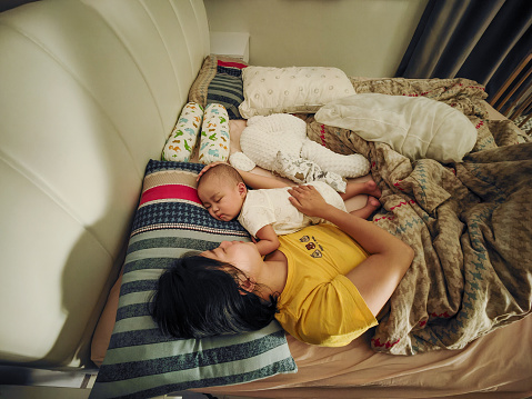 Young Asian mother embracing baby boy and sleeping in bed