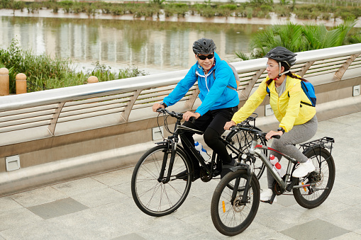 Positive young Vietnamese couple wearing helmets when cycling in city