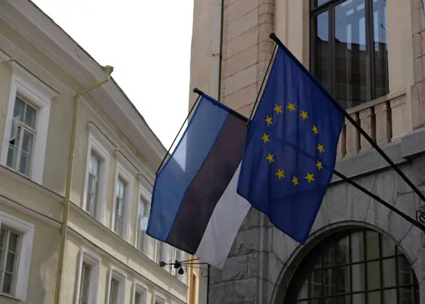 National flag of Estonia and Europe Union flag waving in the wind against of building. Democracy and politics. European country.