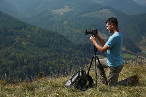 Man taking photo of mountain landscape with modern camera on tripod outdoors