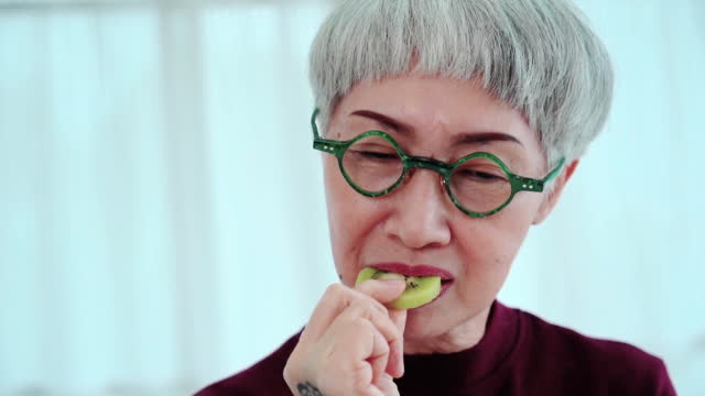 Asain tattooed  senior woman cooking food in kitchen ,  eating kiwi fruit