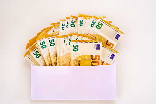 Many fifty euro banknotes stuffed into a white paper envelope, isolated on a white background