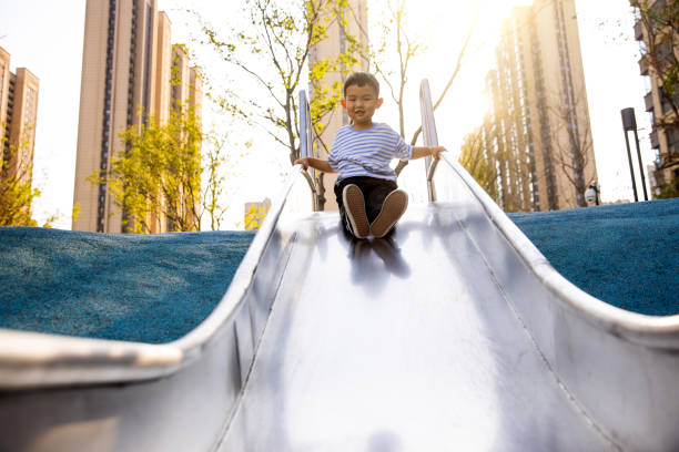 Mixed race boy sliding down slide in playground - Stock Photo
