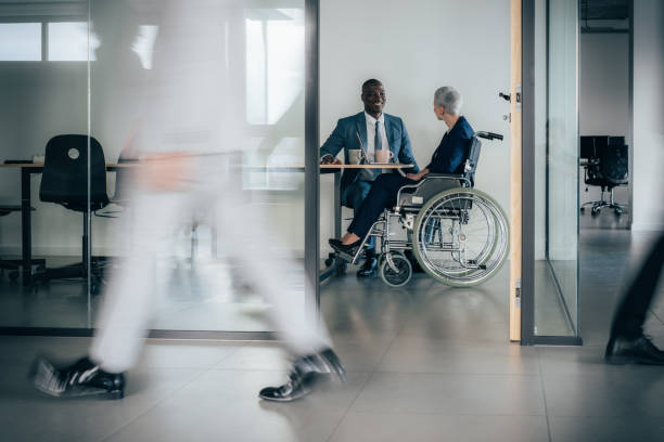 Wheelchair access in the office Business woman in wheelchair having meeting in Busy modern workplace. Working process in the office, business people working, walking and talking, blurred motion accessibility for persons with disabilities photos stock pictures, royalty-free photos & images