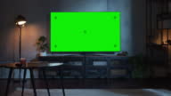 istock Zoom Out Shot of TV with Horizontal Green Screen Mock Up. Evening Living Room at Home with Chroma Key Placeholder on Monitor. No People 1403072786