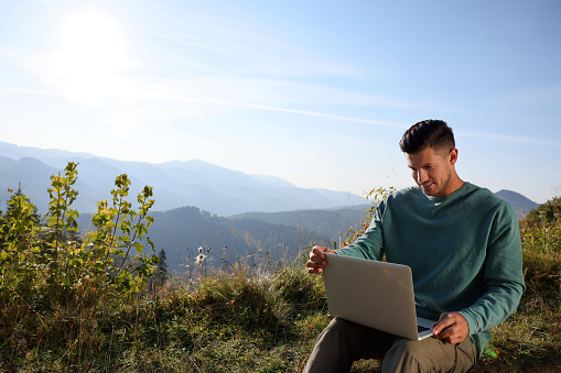 Man working on laptop outdoors surrounded by beautiful nature