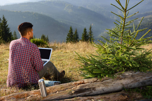 istock Man working on laptop outdoors surrounded by beautiful nature, back view 1403072863