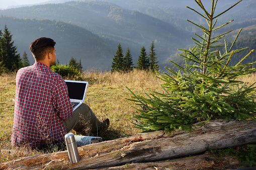 Man working on laptop outdoors surrounded by beautiful nature, back view