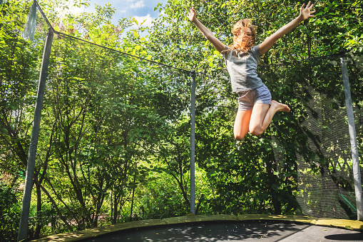 Preteen girl having fun bouncing on a trampoline in a backyard on a summer day