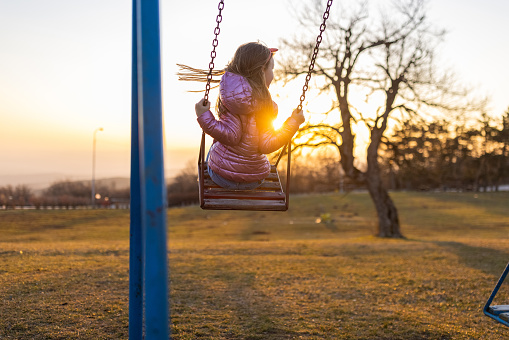 Rear view of unrecognizable Caucasian girl swinging on the swing during sunset
