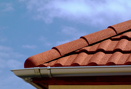 close up of wavy concrete tiled roof ridge. strong sandy texture. zink gutter. blue sky and white clouds. construction concept. house roofing. weather and rain protection concept.