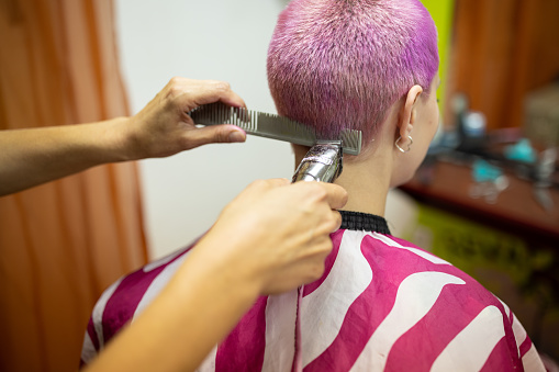 Caucasian female hairdresser, doing hairstyle to a young woman with pink dyed short hair