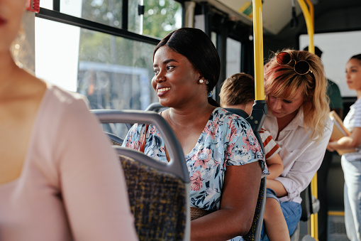 A young black woman is sitting in a public transport looking through the window and smiling