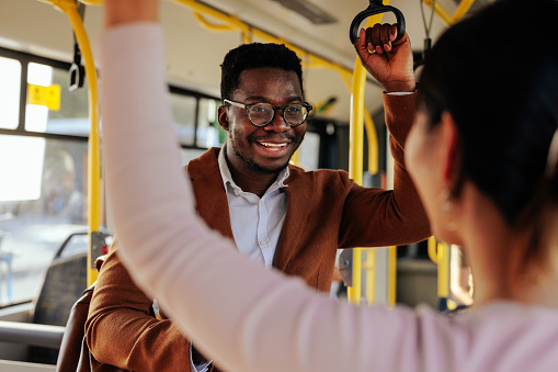 A young african american man is talking to a woman in a public city bus