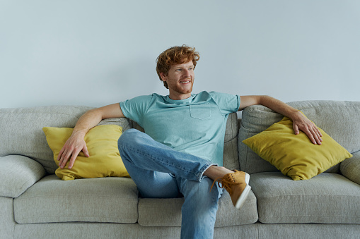 Handsome redhead man smiling while relaxing on the couch at home