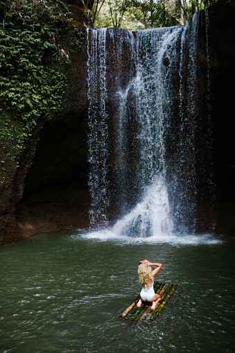 Woman have fun in natural pool under falling water of Suwat waterfall in tropical jungle. Nature day tour, swimming activity adventure and fun at family tourist camp on summer vacation in Bali island.