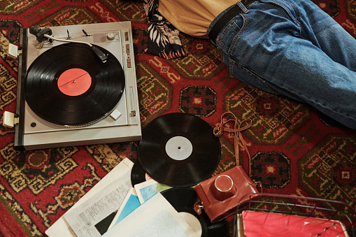Part of young man in blue jeans relaxing on red carpet on the floor and listening to vynil disks with his favorite music