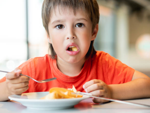 istock Kid in red t-shirt eats food with knife and fork. Fastidious boy with puzzled expression on face. 1403082683