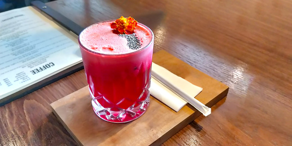 Red strawberry juice with orange flower and pinch of chia seed in the top with straw on wooden platter