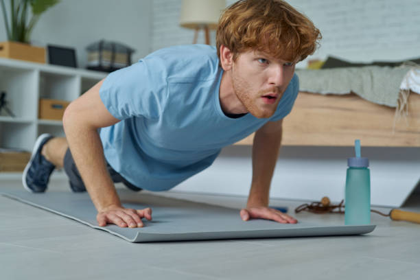 Confident young redhead man doing push-ups at home stock photo