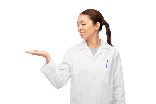 medicine, profession and healthcare concept - happy smiling asian female doctor in white coat holding something invisible on her hand