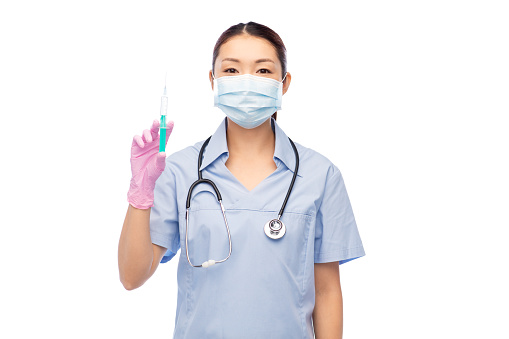 medicine, vaccination and healthcare concept - asian female doctor or nurse wearing face protective medical mask for protection from virus disease with stethoscope and syringe over white background