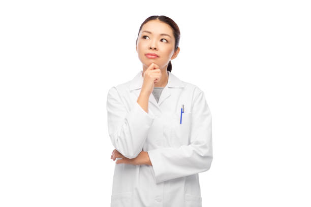 thinking asian female doctor in white coat stock photo