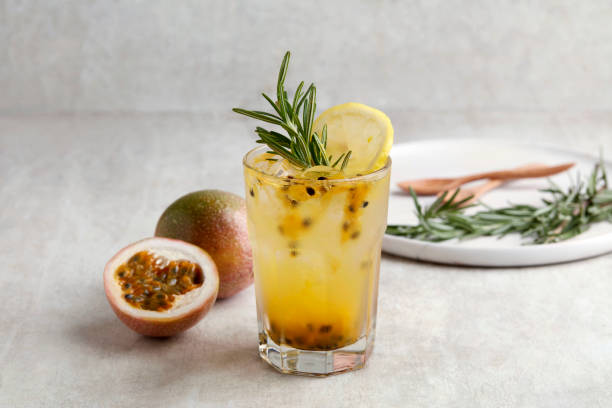 A glass of Iced passion fruit soda with lemon and passion fruit half slice on grey background, a healthy summer drink stock photo
