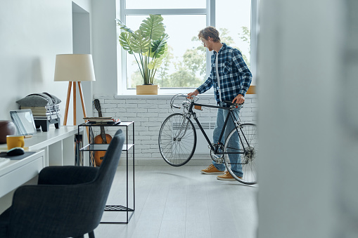 Young man examining his bicycle while standing at the living room