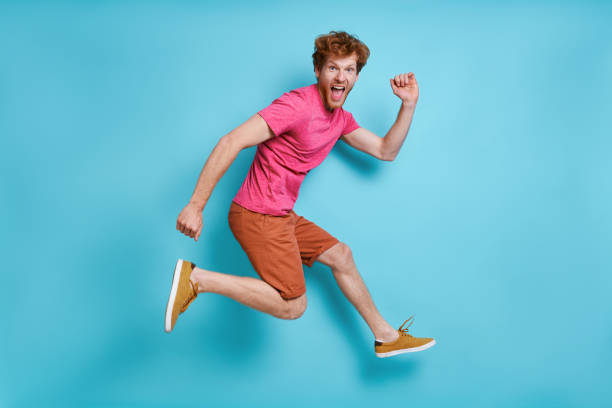 istock Happy young redhead man jumping against blue background 1403087514