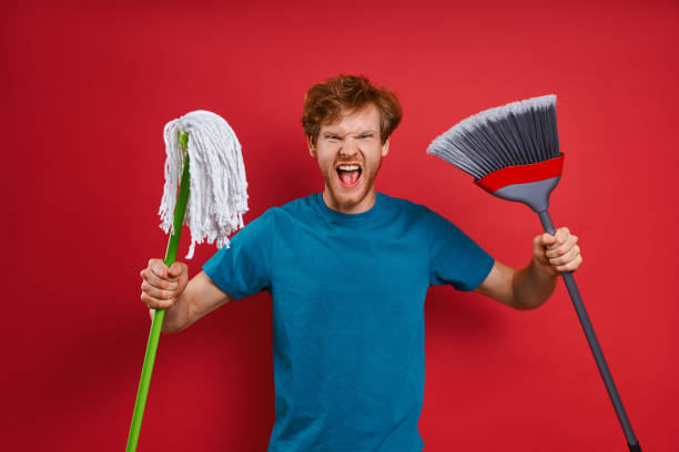 Furious young man carrying cleaning equipment and grimacing stock photo