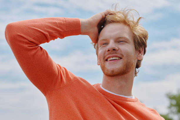 happy young redhead man holding hand in hair and smiling - hand in hair imagens e fotografias de stock