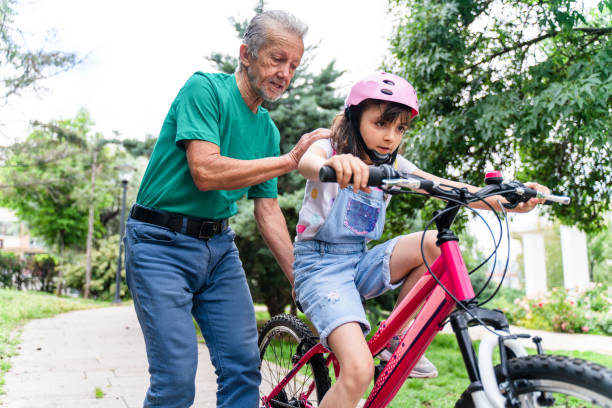 une petite fille apprend à faire du vélo avec grand-père - active seniors enjoyment driveway vitality photos et images de collection