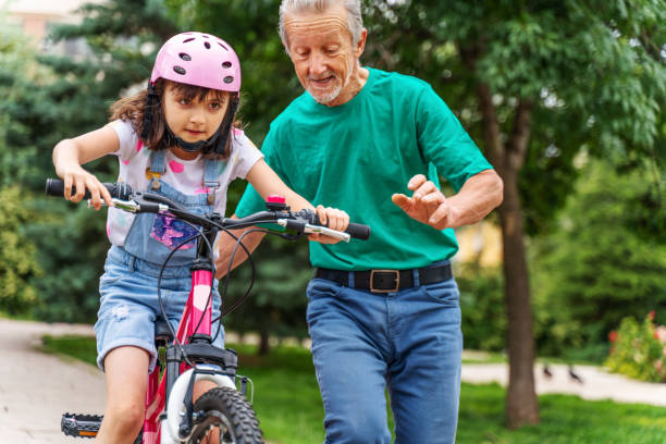 petite fille ride a bike avec grand-père d’apprentissage - active seniors enjoyment driveway vitality photos et images de collection