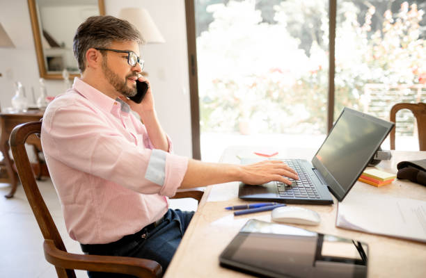 istock Businessman talking on a phone while working from home on a laptop 1403090571