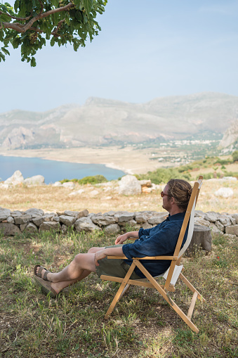 He relaxes in a foldable chair and looks off towards Mediterranean Sea in the distance