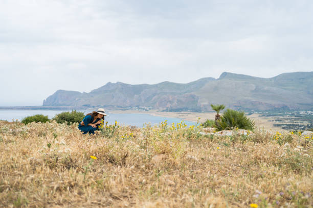 She leans down to smell wildflowers, Mediterranean Sea in the distance