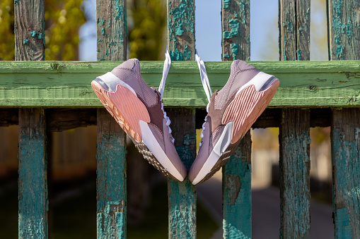 pink new sneakers hang on laces on an old green wooden fence