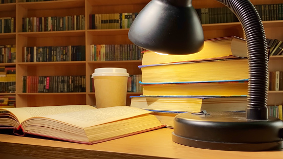Stack of books on wooden desk in the library room background. Education and knowledge concept. Pile of books to read.