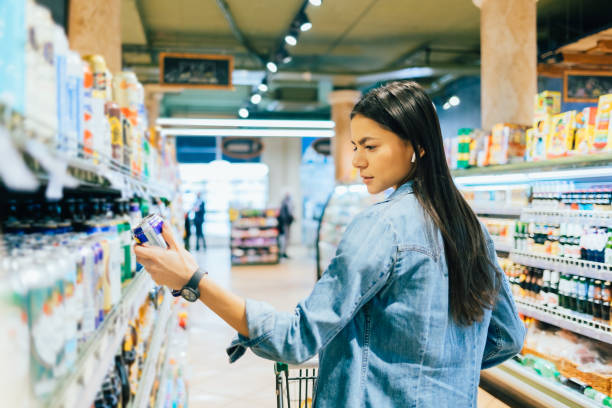 Young woman buying beer or ale alcohol in liquor store Young woman buying beer or ale alcohol in liquor store, standing in front of shelf, holding can reading label grocery shelf cans stock pictures, royalty-free photos & images
