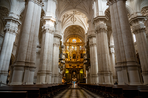 Wide-angle shot of the altar and the stained glass windows protected by the lateral columns of the Cathedral of Granada in Spain was taken from the main entrance