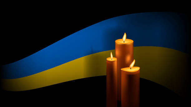istock Ukrainian flag ribbon and three burning wax candles with shadow on black background. Commemorative banner of day of remembrance of dead. 1403102171
