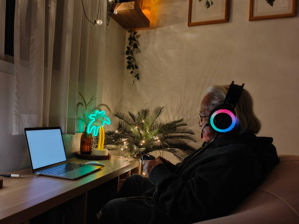 Asian senior woman playing computer game on laptop at night stock photo