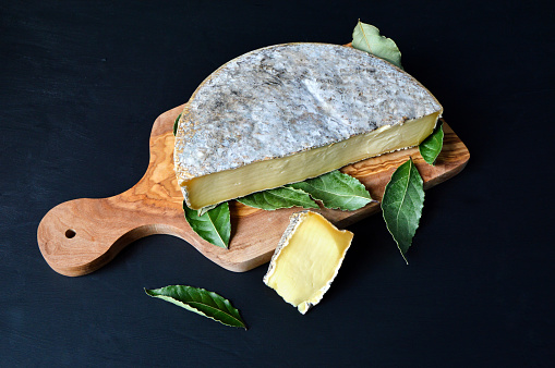 Saint Nectaire cheese with bay leaf on a cutting board. It is an Auvergne cheese and a mountain cheese made with cow’s milk.