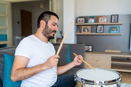 A mature man in casual clothes plays acoustic drums in her room.