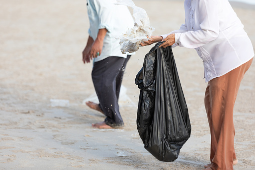 volunteer keeping and picking trash into garbage bag on the beach