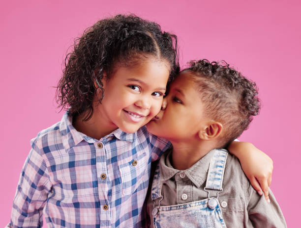 istock Two children only posing and being affectionate against a pink copyspace background. African American mixed race siblings kissing while bonding in a studio 1403107880