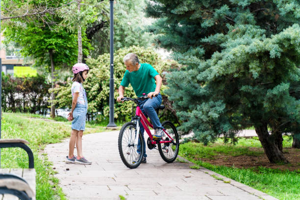 little girl learning ride a bike with grandfather - active seniors enjoyment driveway vitality imagens e fotografias de stock