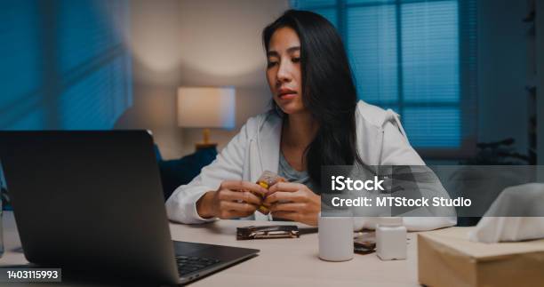 Sick Young Asian Woman Using Laptop Talk To Doctor In Living Room At Home At Night Stock Photo - Download Image Now